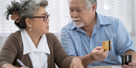woman and man sitting at table. man holding credit card, woman writing on piece of paper