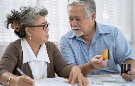 How-to-pay-off-credit-card-debt-feature woman and man sitting at table. man holding credit card, woman writing on piece of paper