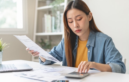 woman holding piece of paper and tapping on calculator
