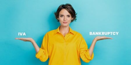 woman wearing yellow jumper holding out hands either side of her like scale. Text on one hand reads IVA, text on other hand reads Bankruptcy.
