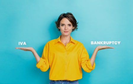 Whats-the-differnce-between-iVA-and-bankruptcy_-feature woman wearing yellow jumper holding out hands either side of her like scale. Text on one hand reads IVA, text on other hand reads Bankruptcy.