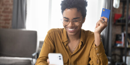 How-to-stop-overspending-feature Woman holding a blue credit card smiling at her mobile