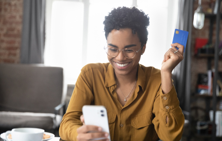 Woman holding a blue credit card smiling at her mobile