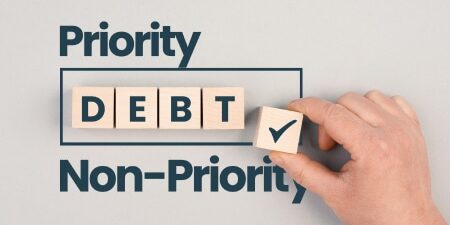 Grey background with the text "Priority Debt and Non-Priority' with some wooden blocks displaying "Debt"