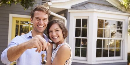 10-Ways-to-Increase-Your-Chances-of-Getting-a-Mortgage-in-2024-feature A couple standing outside of their new house, smiling with a set of keys