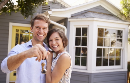 10-Ways-to-Increase-Your-Chances-of-Getting-a-Mortgage-in-2024-feature A couple standing outside of their new house, smiling with a set of keys