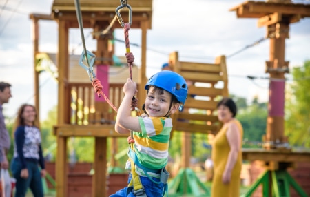 Cheap-or-Free-Activities-for-the-Kids-feature A child on a zipwire at a playground with family in the background