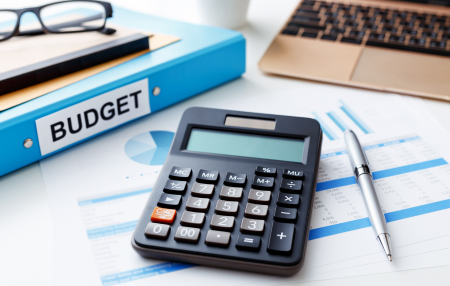 Image of a calculator, pen, laptop, reading glasses and a blue folder titled "budget."