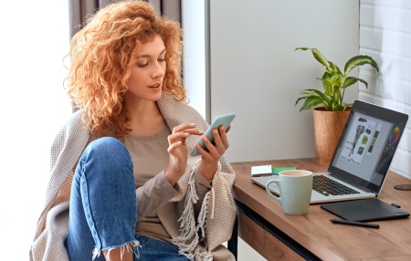 Can-Side-Hustles-Pay-Off-Debt_-feature A woman sat at her desk looking on her phone.