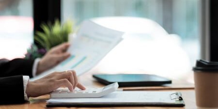 The Success of Debt Management Plans feature An image of someone typing on their calculator at their desk whilst holding a piece of paper