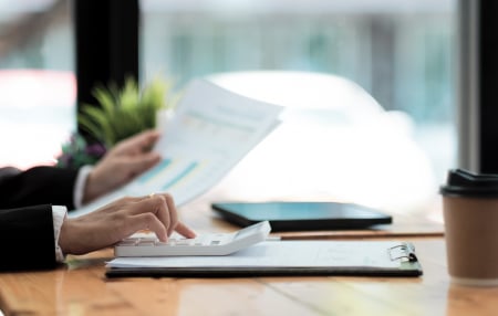 An image of someone typing on their calculator at their desk whilst holding a piece of paper