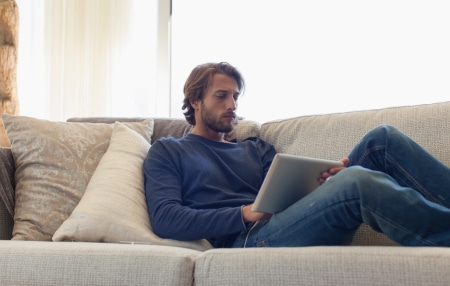 Image of man laying on the sofa looking at his iPad