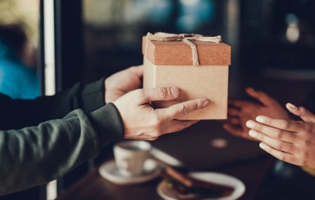 How-to-Manage-Gift-Giving-Expectations-While-in-Debt-feature An image of someone passing a wooden gift box to their friend.