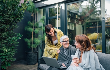 Image of a granddaughter, mother, and grandmother all sitting outside, smiling, with a laptop.