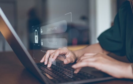 What-Is-Identity-Theft-feature-1 Image of someone typing on their laptop with the screen requesting their username and password.