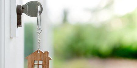 can-you-get-a-mortgage-with-debt-feature Image of a key in a front door with a wooden house keychain attached