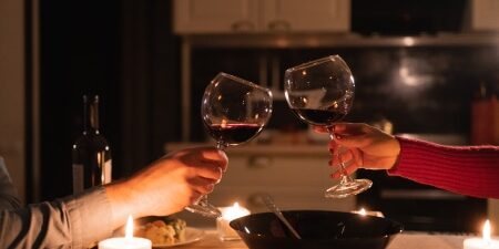Dating on a budget_ 13 cheap – yet romantic – date ideas feature Image of a couple clinking their wine glasses together filled with red wine over a candlelit dinner