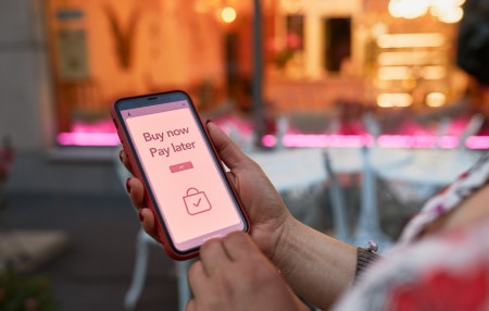 Rise of Buy Now Pay Later schemes feature Image of someone looking at their mobile with the words 'Buy Now Pay Later' displayed