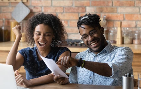 Top Tips to Help You Get Debt-Free feature Image of a couple sitting at their table with their laptop, smiling at sheets of paper.