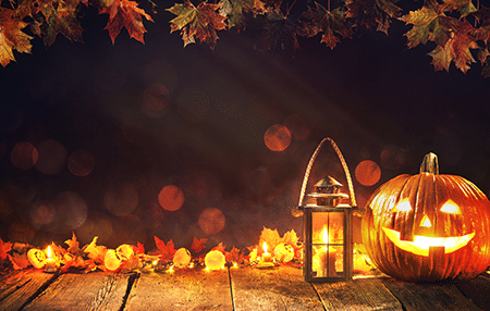 Image of a pumpkin lit up and a lantern on a dark background with autumn leaves