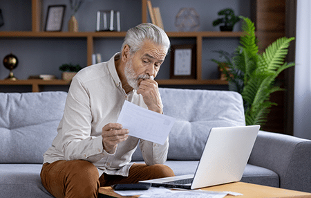 How to overcome debt depression (feature) Image of an older man sitting on his sofa reading a letter with his laptop.