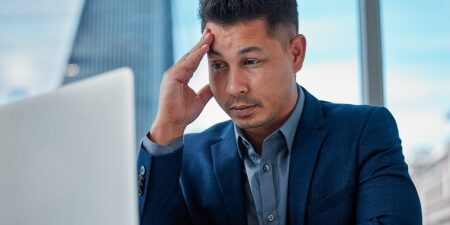 Stress Awareness Day_ Ways to Reduce Debt and Worry feature Image of a man with his head in his hands looking at his laptop screen