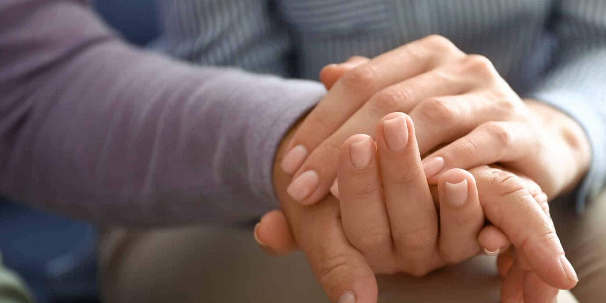 a close up of a young woman’s hand holding the hand of an elderly person.