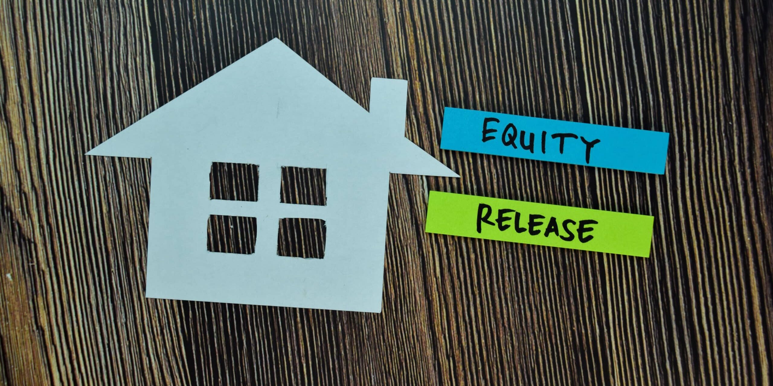A paper house cutout next to labels reading "Equity" and "Release" on a wooden background.