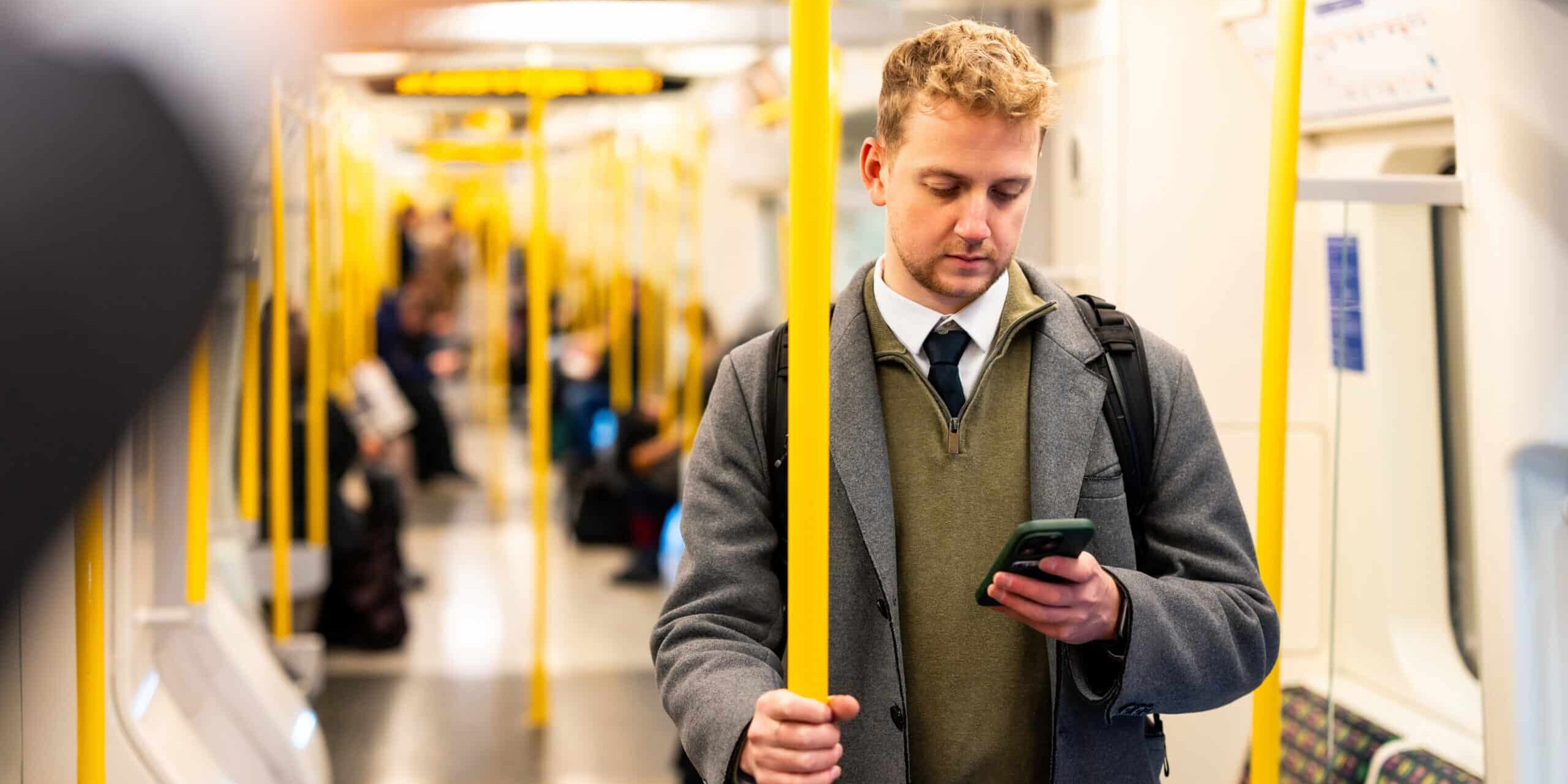 Young businessman holding onto a pole while using his smartphone inside a moving subway train, navigating the bustling urban environment during the morning commute