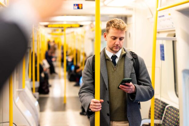 Young businessman holding onto a pole while using his smartphone inside a moving subway train, navigating the bustling urban environment during the morning commute
