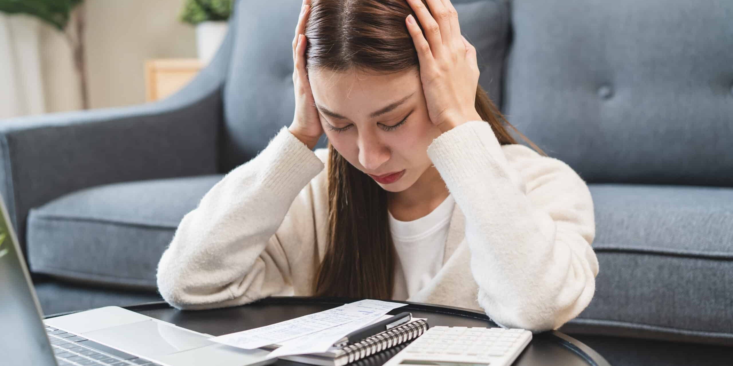 Worried woman looking at bills with a laptop and calculator on the table.