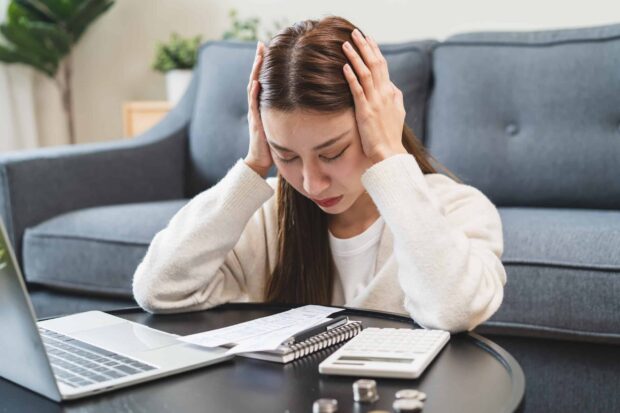 Worried woman looking at bills with a laptop and calculator on the table.