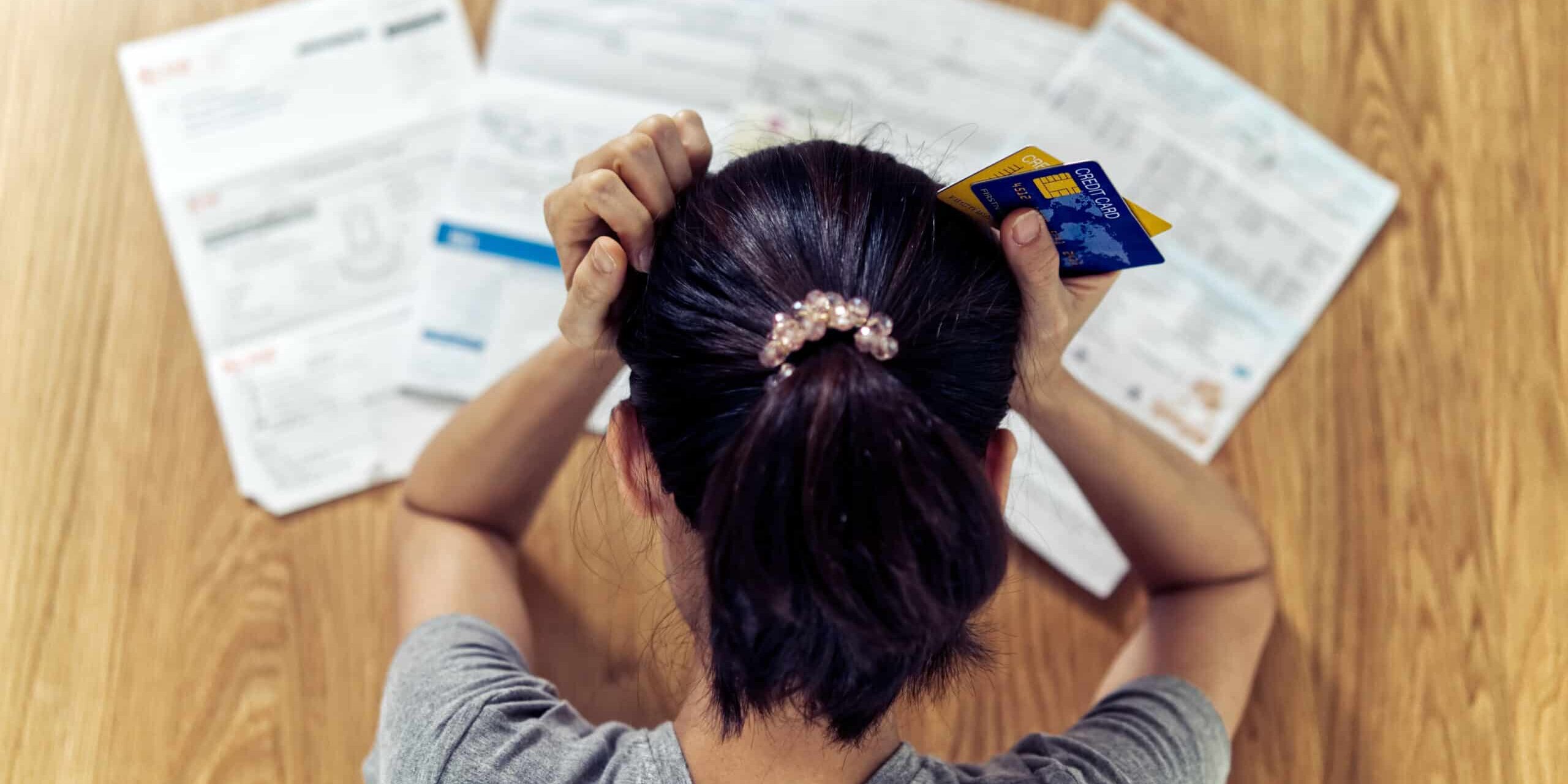Woman holding credit cards, stressed over bills on a table.