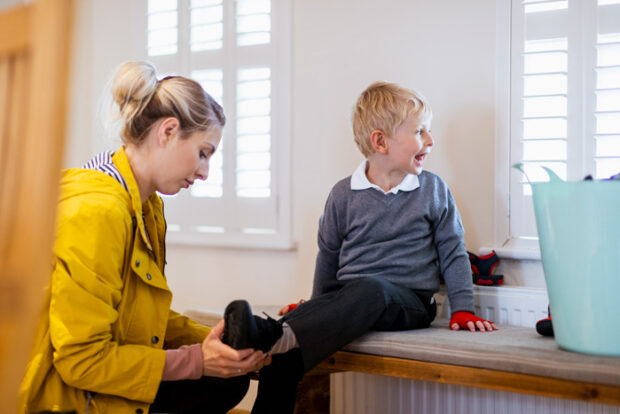 A wide shot of a Caucasian, mother helping her son put his shoes on before school.